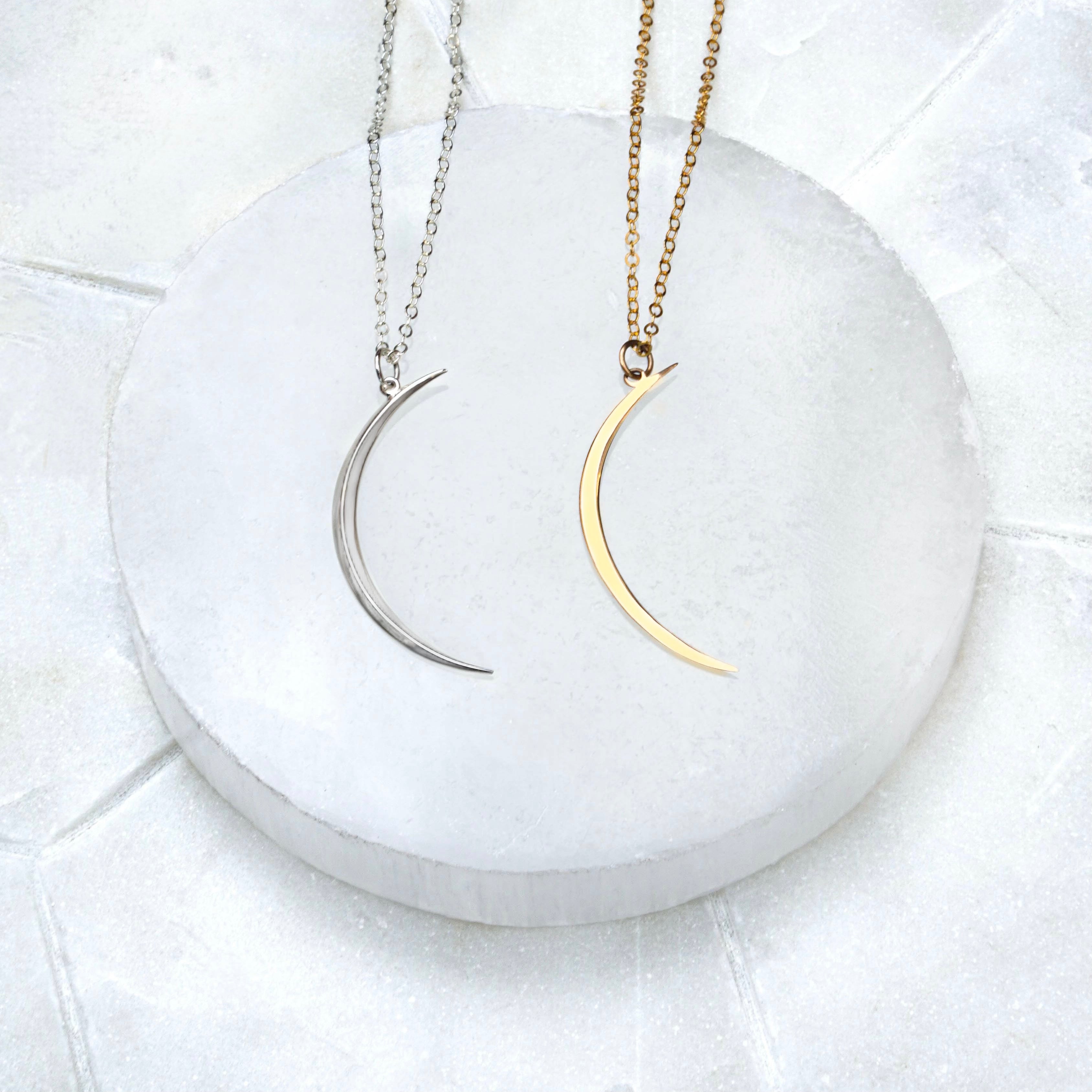 Two Luna Moon Necklaces, one sterling silver and the other in gold fill, displayed on a marble surface.
