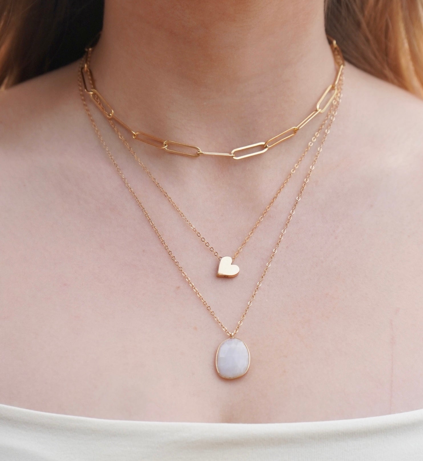 Small moonstone f acceded bezel set pendant shown with a simple heart charm necklace and a paperclip chain choker.