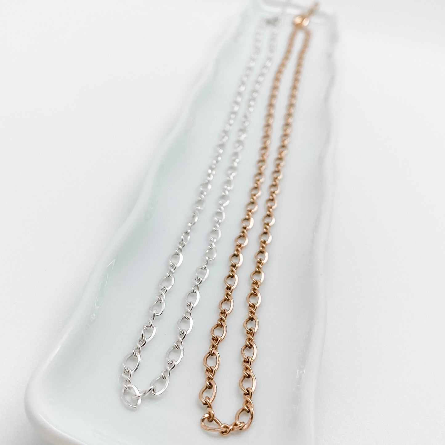 Two necklaces, one silver and one gold, laid out on a white surface, representing classic link chains.