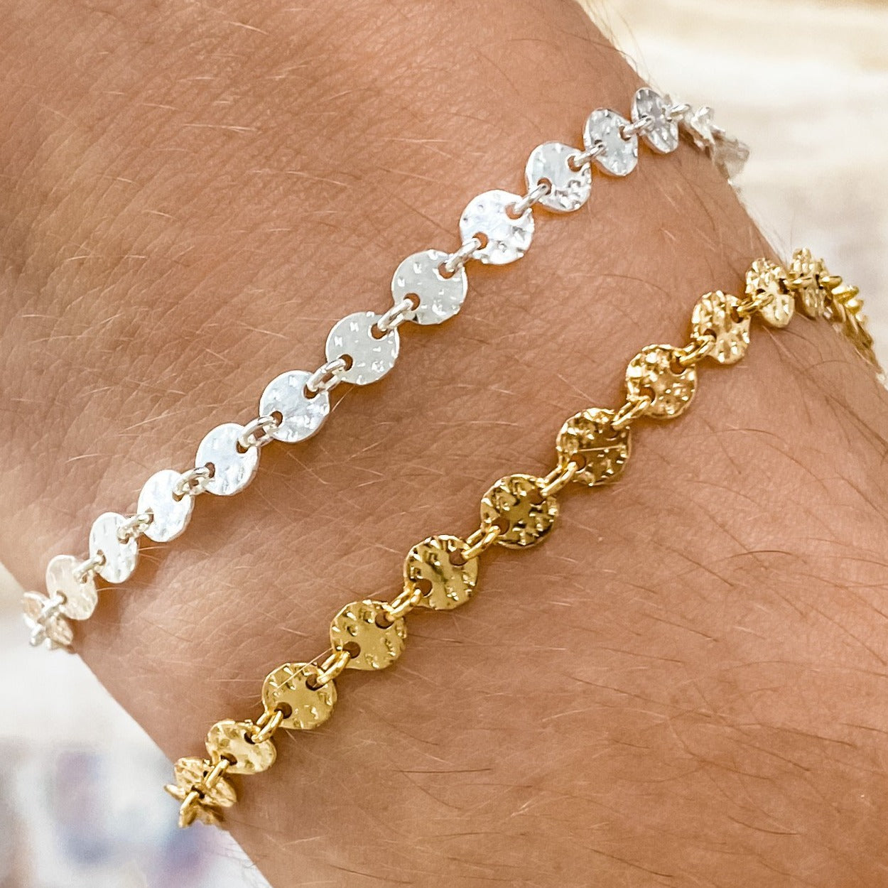 Two bracelets on a wrist, one with a silver coin pattern and the other with a gold filled coin pattern.
