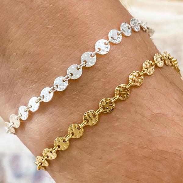Two bracelets on a wrist, one with a silver coin pattern and the other with a gold filled coin pattern.