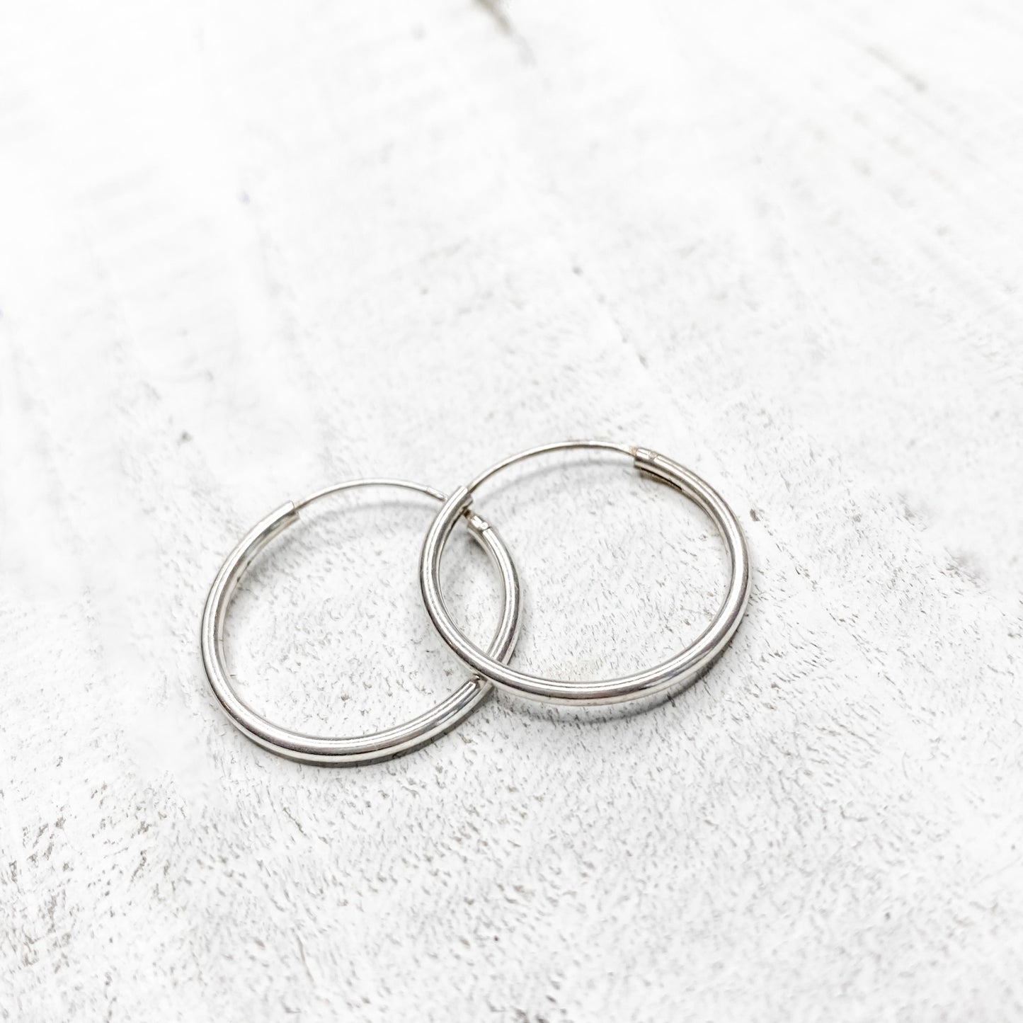A pair of silver-colored hoop earrings placed on a textured surface.